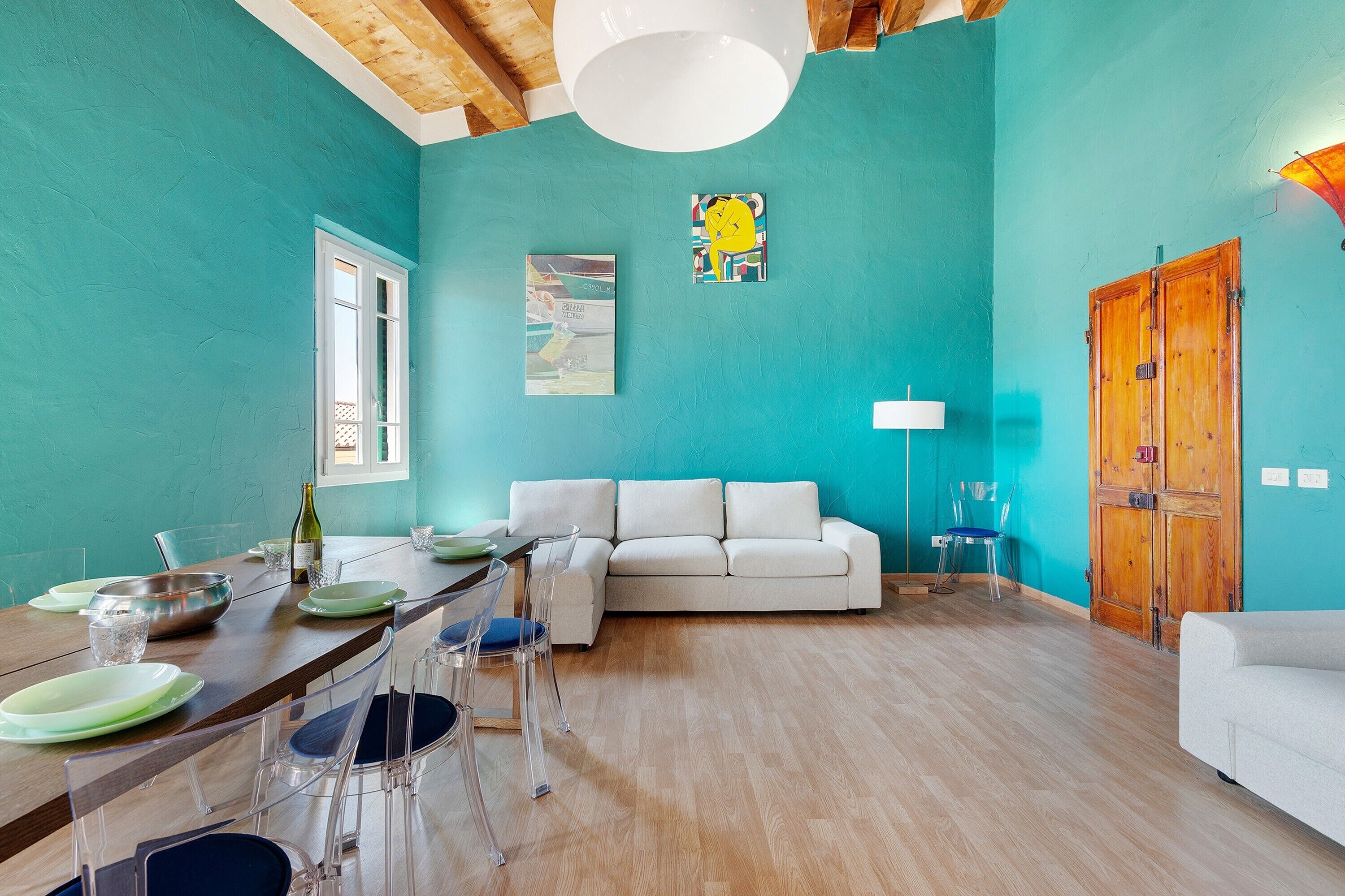 Amplia sala de estar con techo de madera, un sofá blanco, una mesa de comedor con sillas y una puerta de madera.