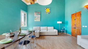 Amplia sala de estar con techo de madera, un sofá blanco, una mesa de comedor con sillas y una puerta de madera.