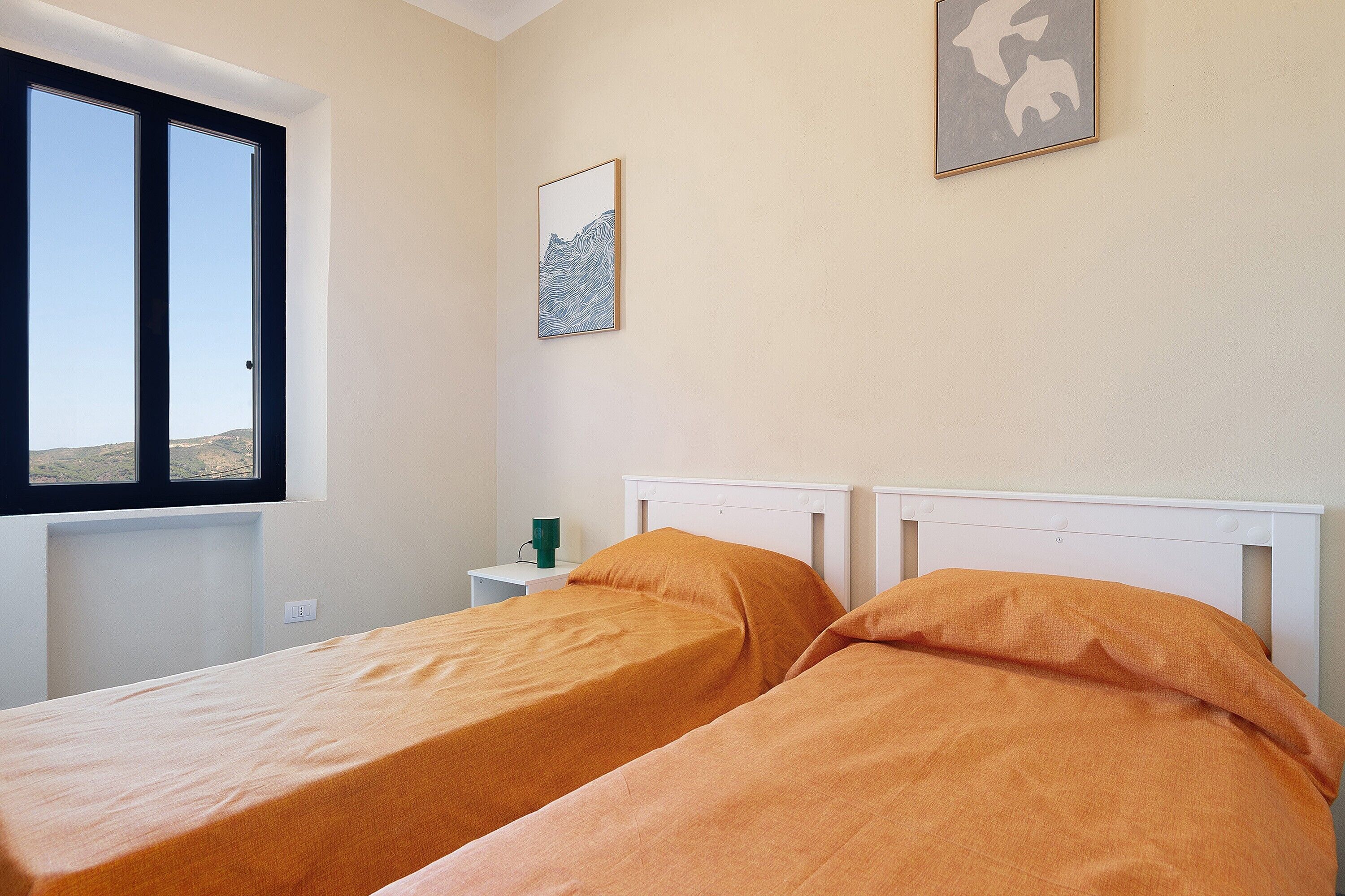 Una camera da letto con due letti singoli, una finestra, un comodino con una lampada e un quadro appeso al muro.