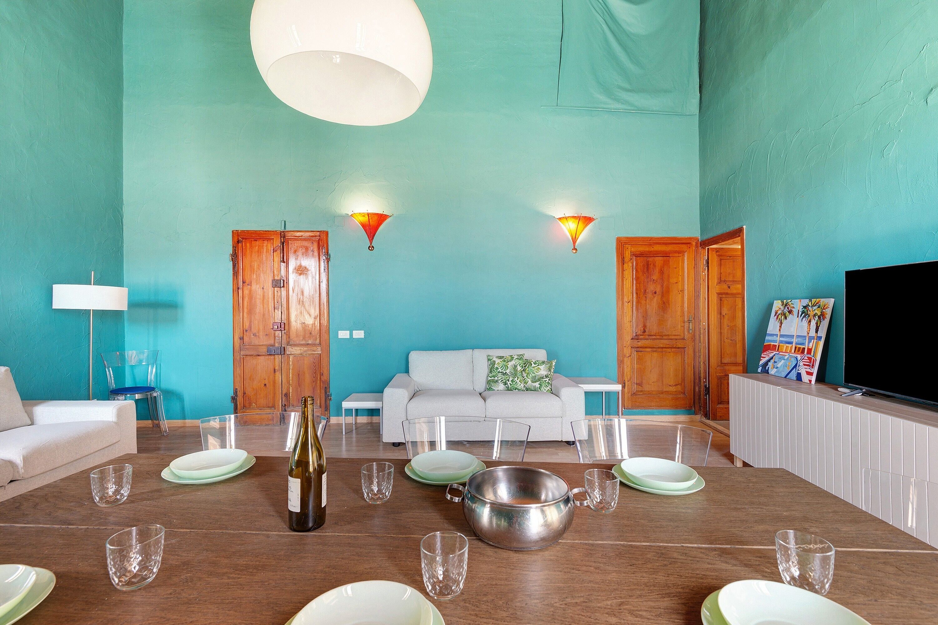 A living room with teal walls, a sofa, a dining table set with plates and glasses, and a television.