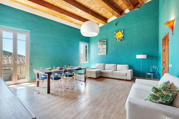A spacious living area with a dining table, chairs, a sofa, and a large window.
