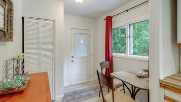 A room with a white door, a window with red curtains, a table with chairs, and a mirror with an ornate frame.