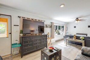 A living room with a large flat-screen TV, a dark wooden cabinet, a blue chair, a coffee table with a decorative bowl, and a grey sofa.