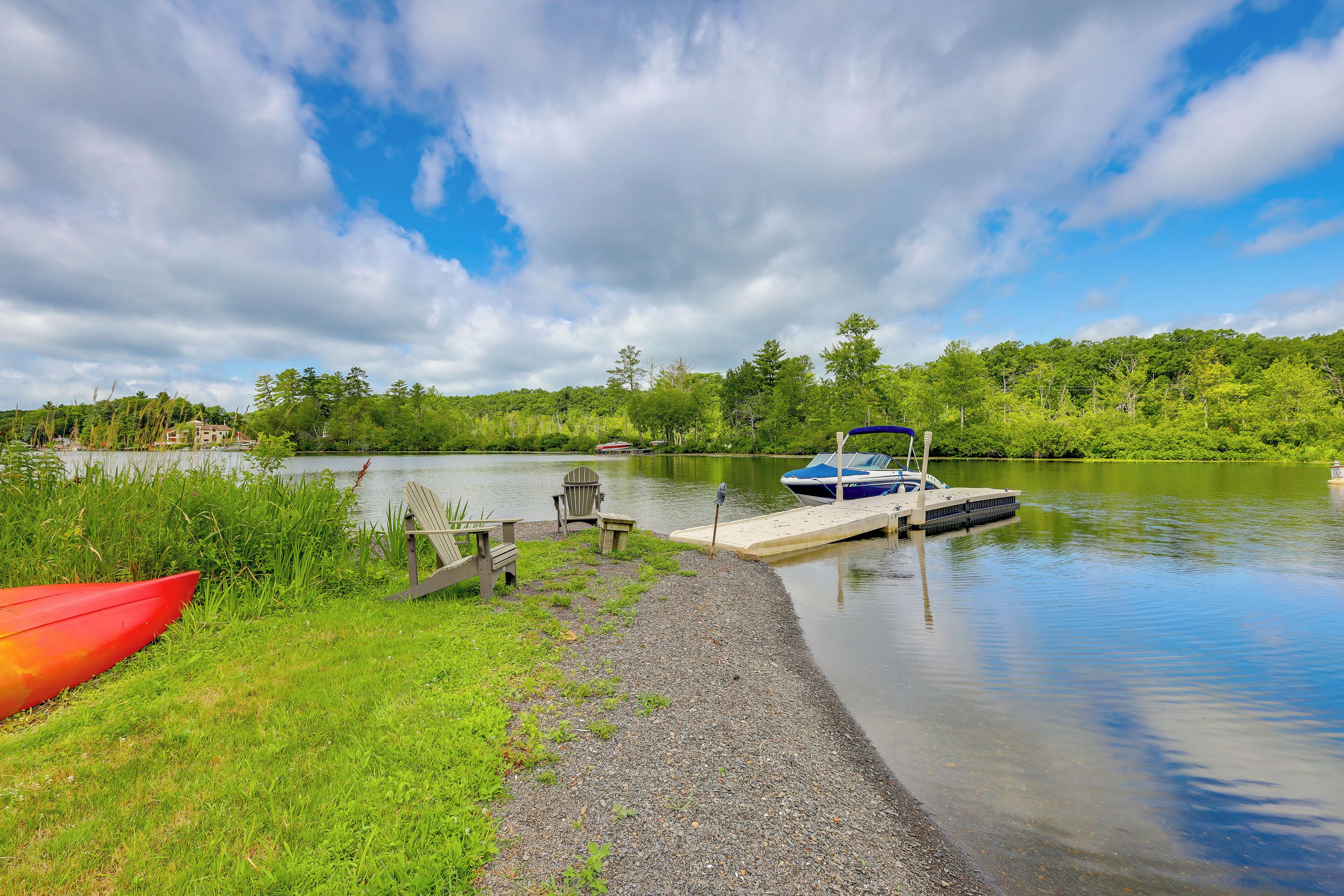 A calm lake with a dock, a red canoe, and a boat.