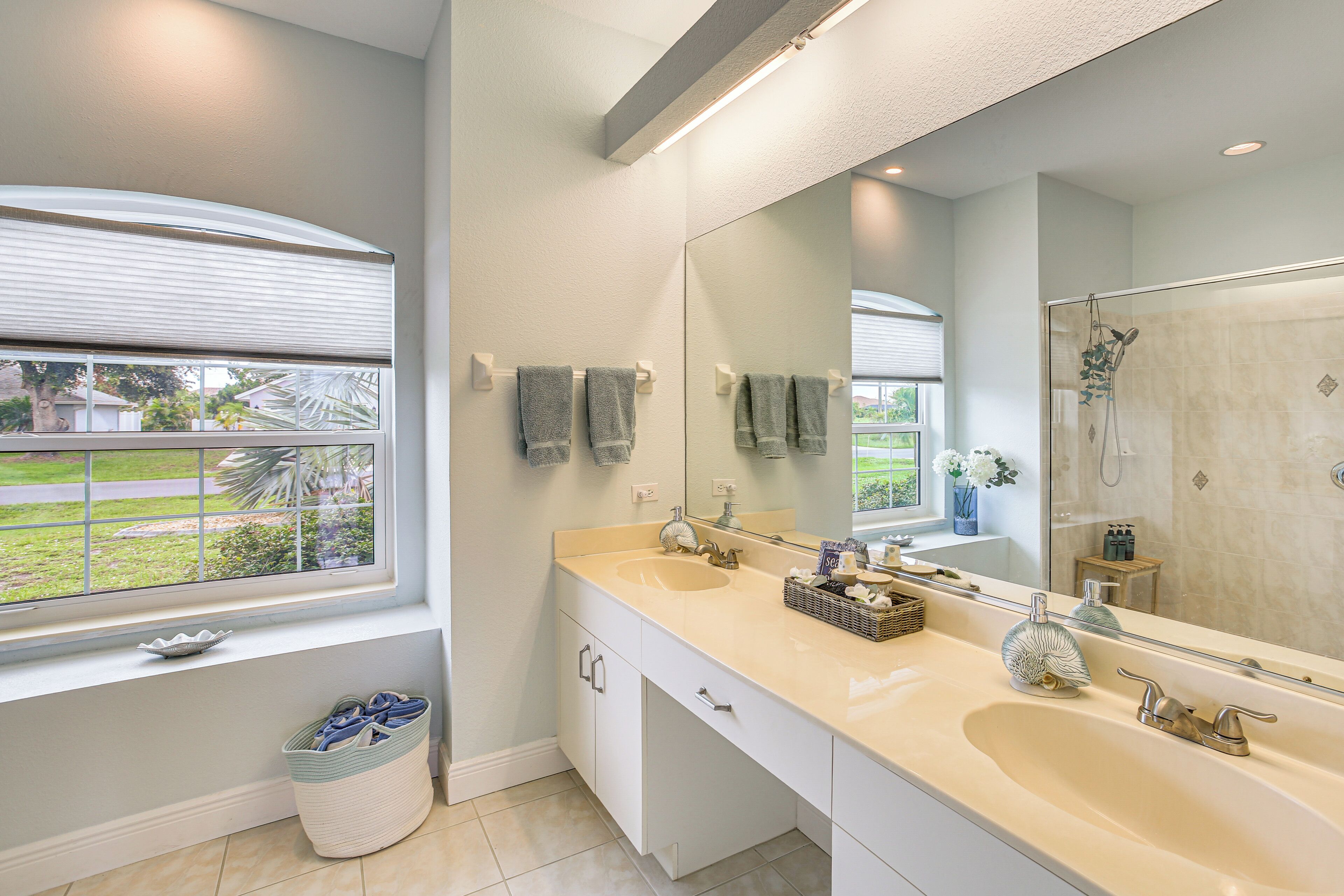 A bathroom with a large mirror, dual sinks, and a window with a view of greenery.