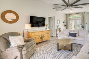 Ein Wohnzimmer mit Fernseher, Deckenventilator, Sofa, Couchtisch und einem gemusterten Teppich.