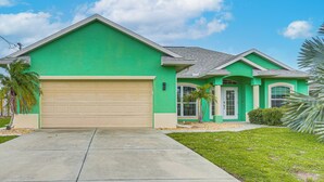 A residential house with a green facade, a beige garage door, and a clear sky. - 8 Mi to Englewood Beach! Canal-Front Family Haven (Rotonda West)