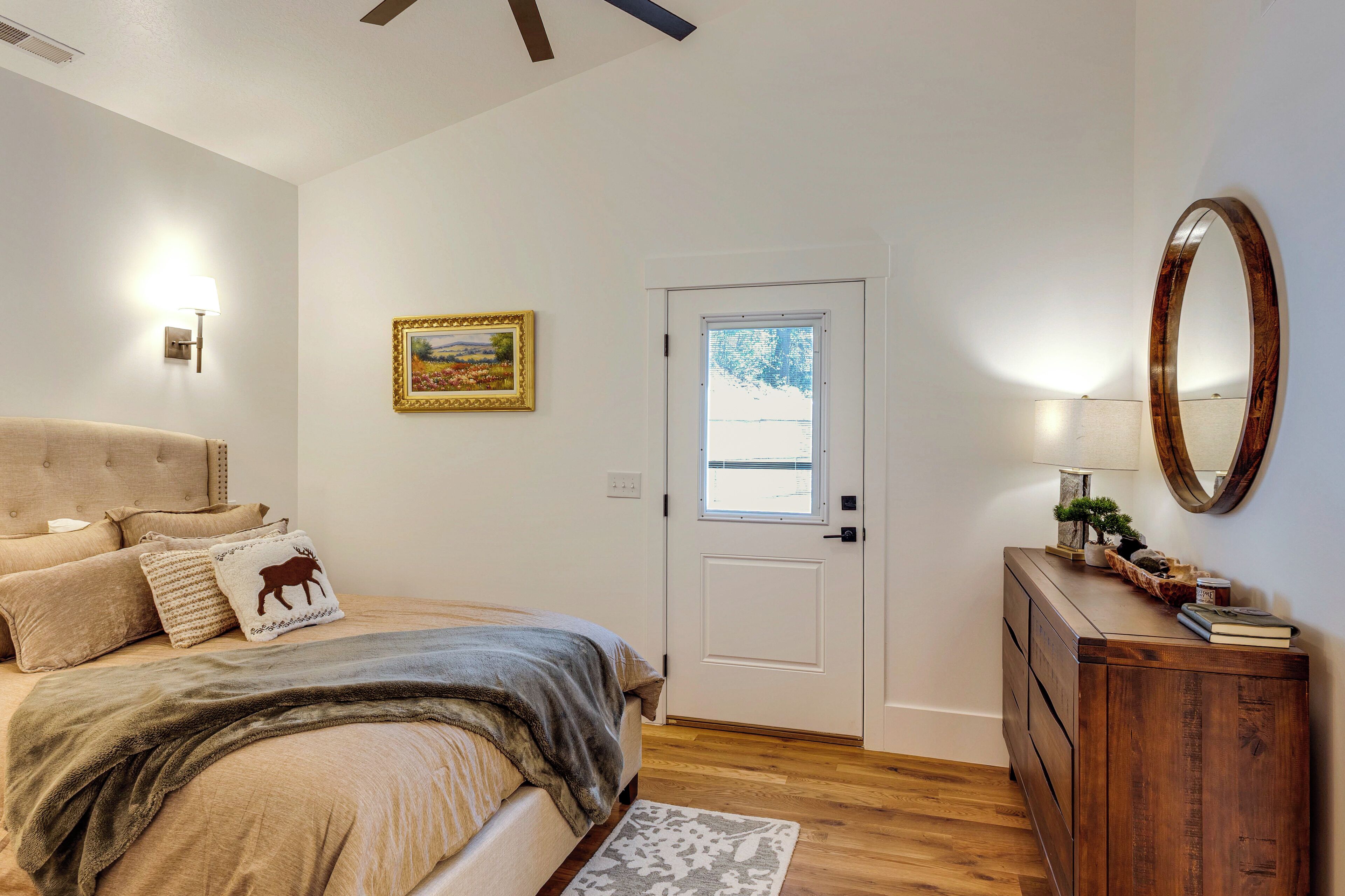 A bedroom with a bed, a dresser, a mirror, a door, and a painting on the wall.