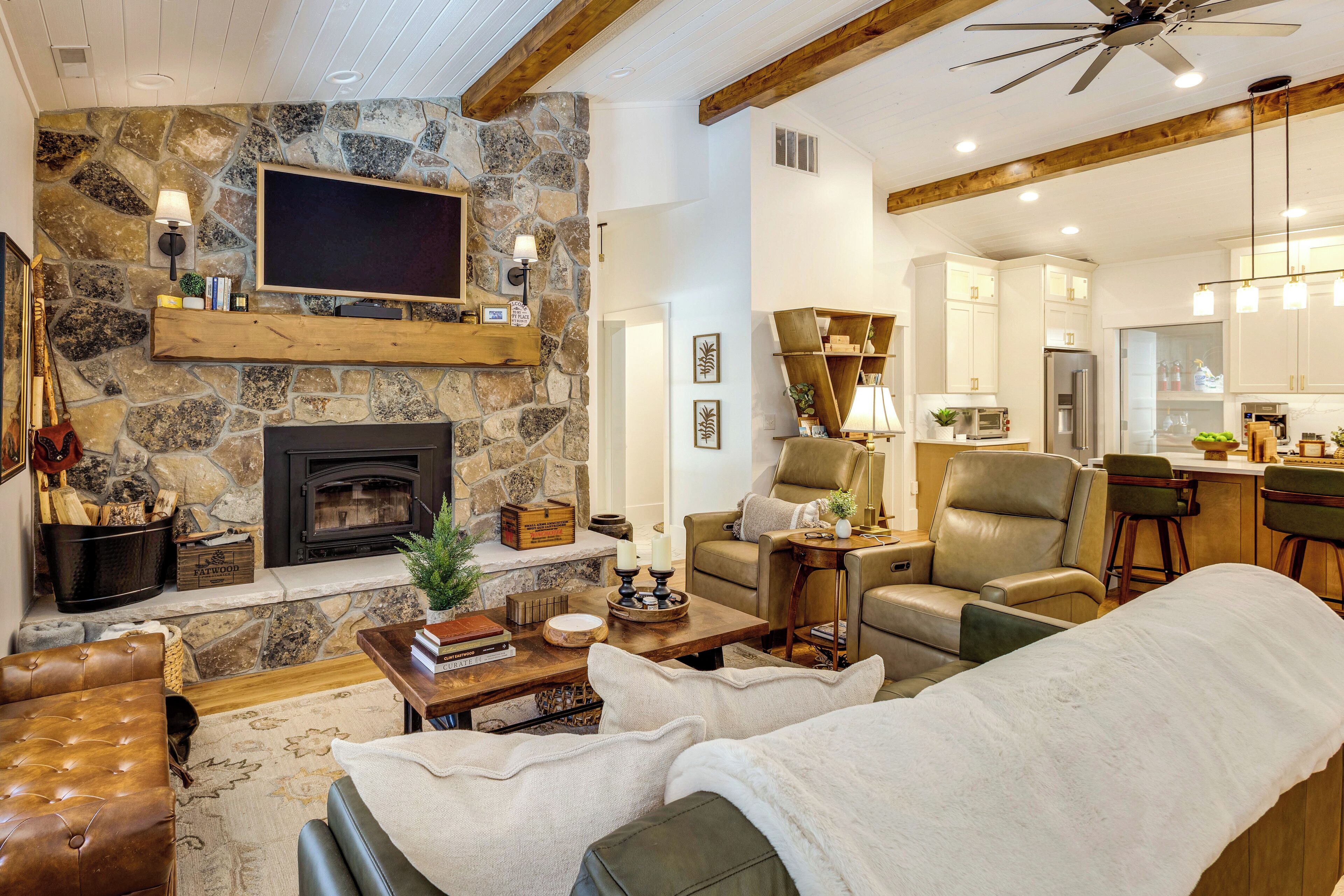 A cozy living room with a stone fireplace, leather sofa, and a television mounted on the wall.