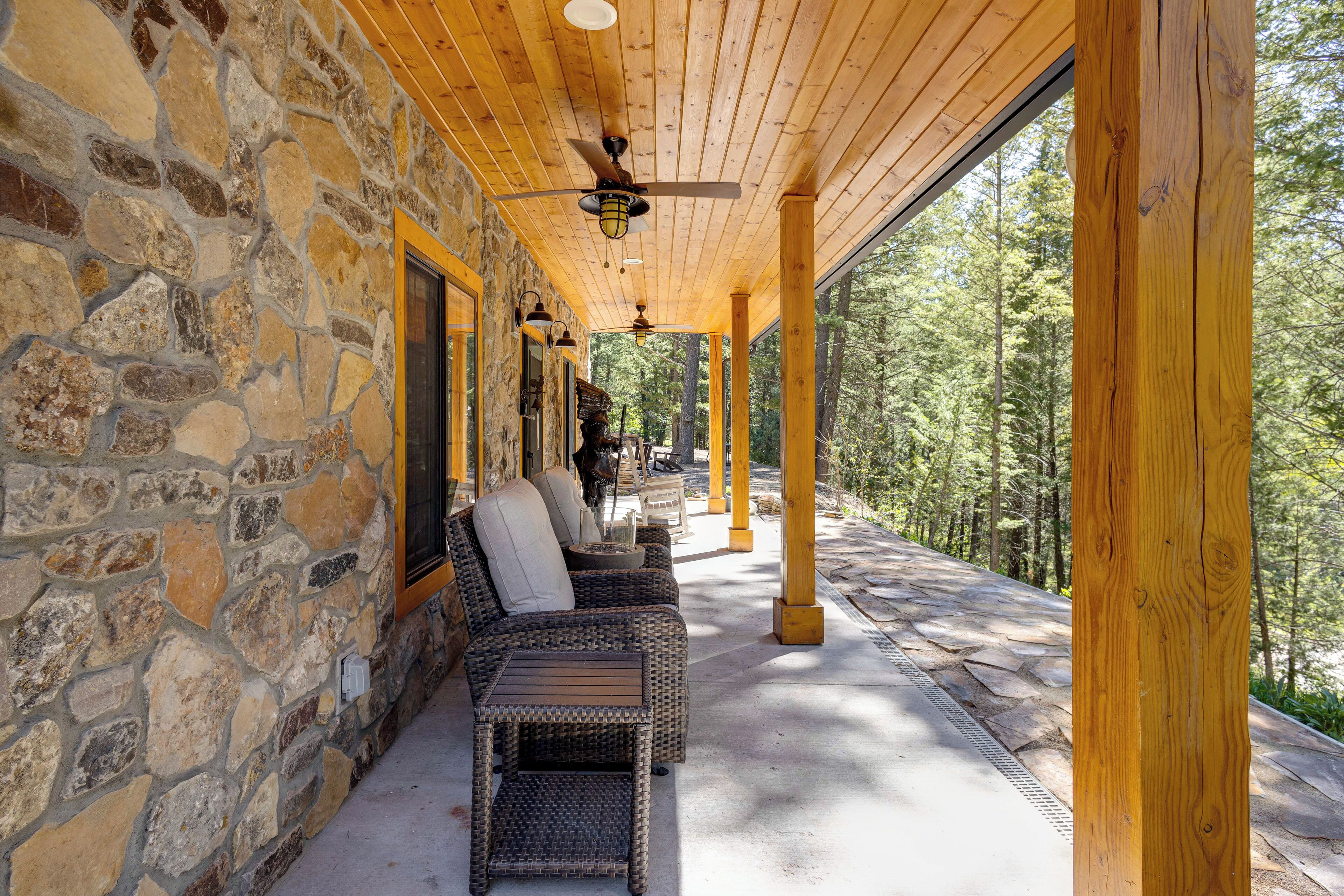A covered outdoor seating area with stone walls, wooden beams, and a view of a forest.