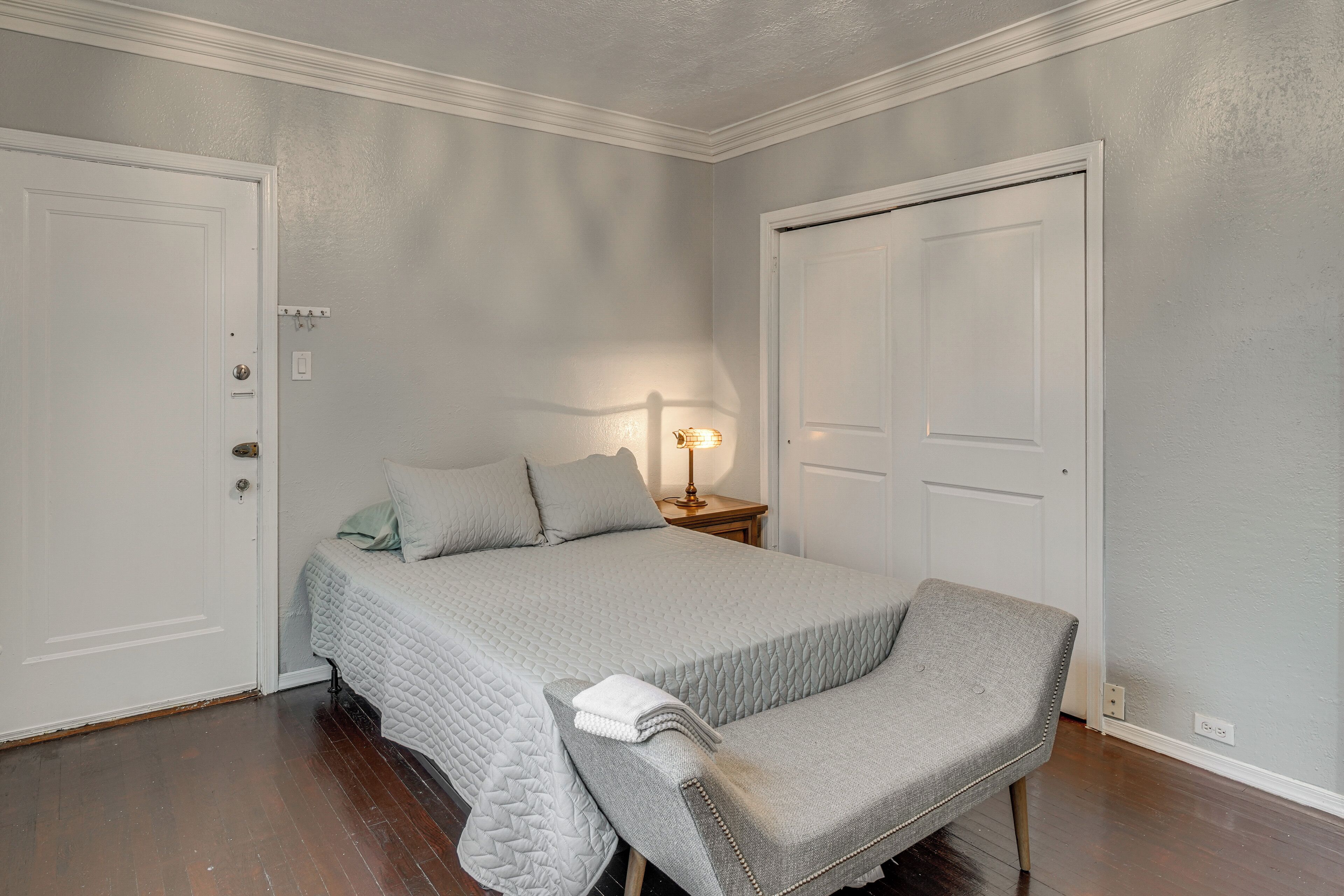 Un dormitorio con una cama, una mesita de noche, una lámpara y dos puertas.