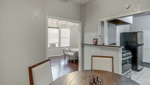 Un comedor con mesa y sillas de madera, una cocina con refrigerador y estufa, y una ventana con persianas.