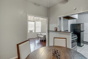 Ein Essbereich mit einem Holztisch und -stühlen, eine Küche mit Kühlschrank und Herd sowie ein Fenster mit Jalousien.