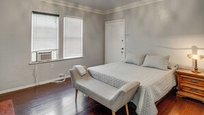 Un dormitorio con cama, una banca, una mesita de noche, una lámpara y una puerta.
