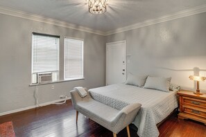 Ein Schlafzimmer mit einem Bett, einer Bank, einem Nachttisch, einer Lampe und einer Tür.