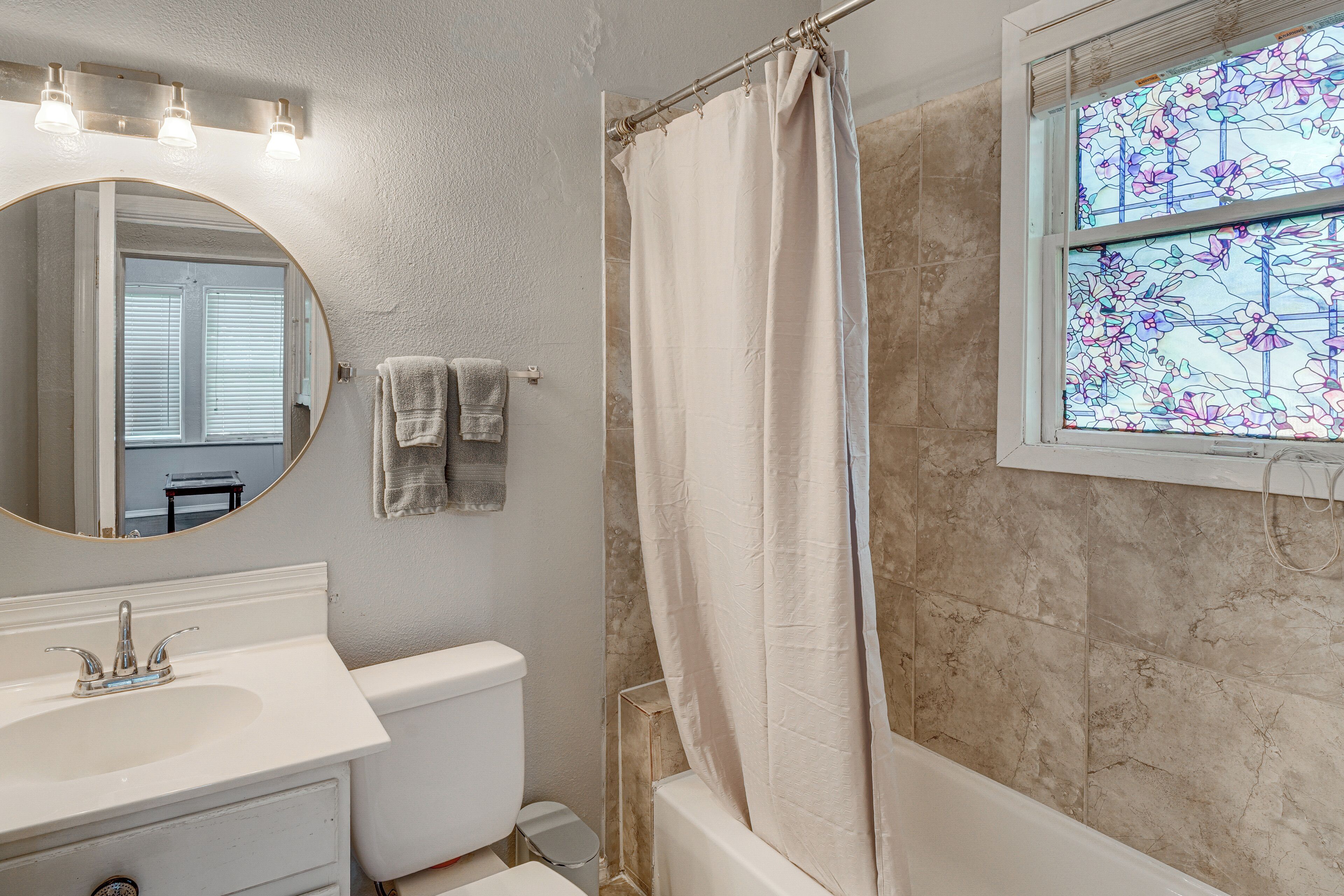 A bathroom with a white vanity, a toilet, a shower curtain, and a stained glass window.