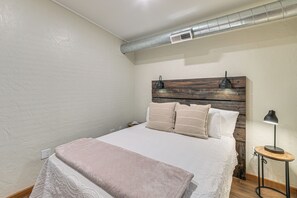 Een slaapkamer met een bed, nachtkastje, lamp en hoofdbord.