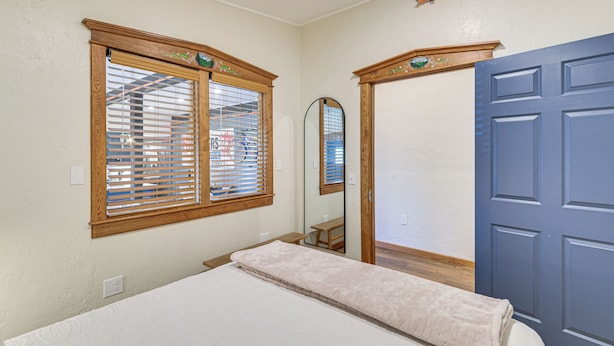 Ein Zimmer mit einem Bett, einer Holztür und einem Fenster mit Jalousien.