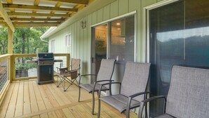 Een overdekte veranda met een barbecue, buitenmeubels en uitzicht op het interieur van het huis.