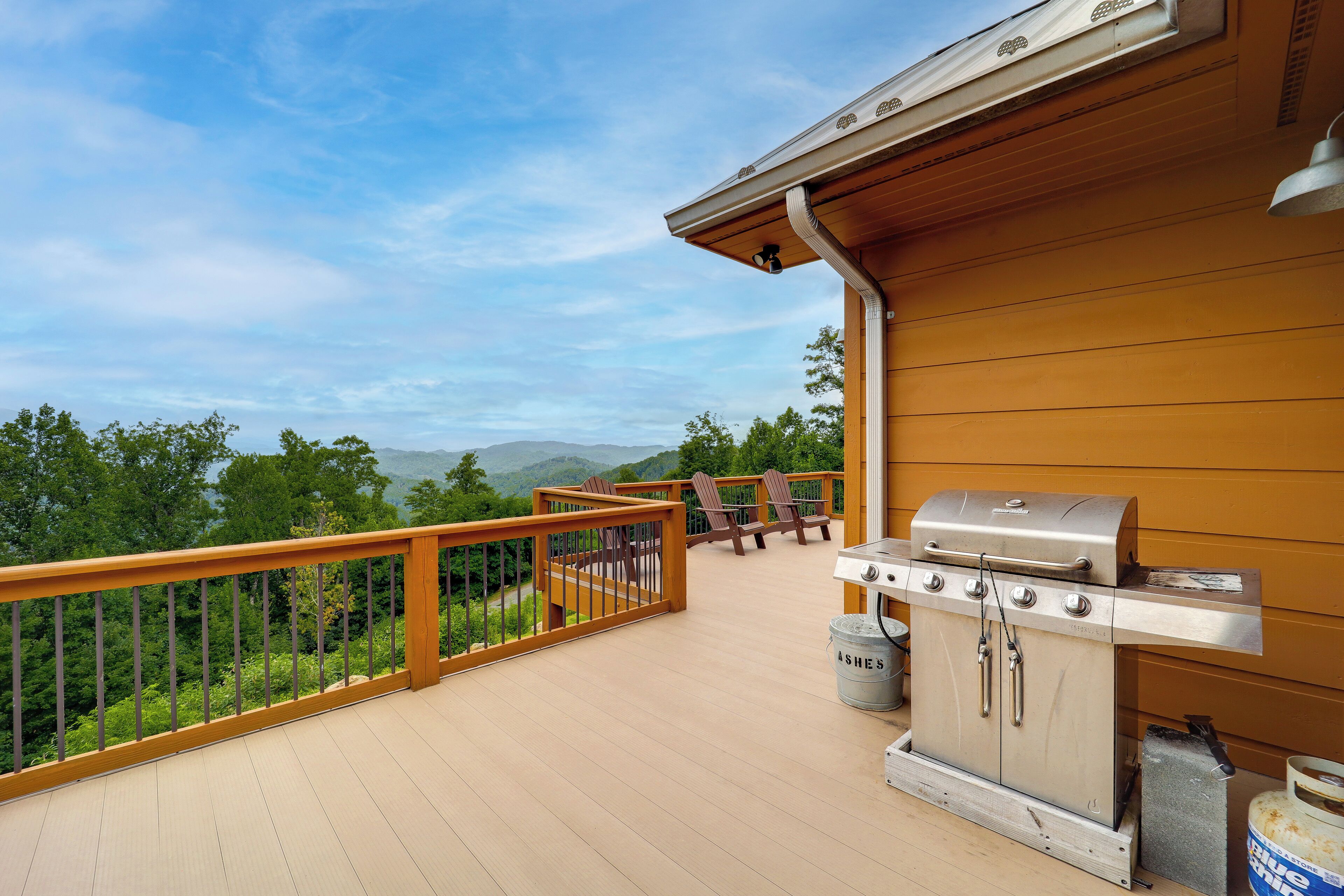 Una terraza de madera con una parrilla y sillas, con vistas a un paisaje montañoso.