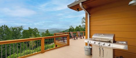 Eine Holzterrasse mit Grill und Gartenmöbeln, mit Blick auf eine Berglandschaft.