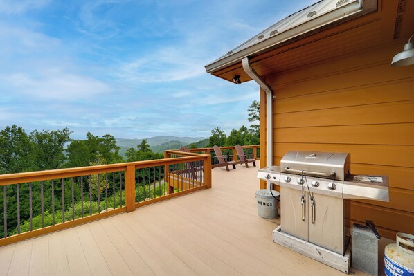 Una terraza de madera con una parrilla y sillas, con vistas a un paisaje montañoso.