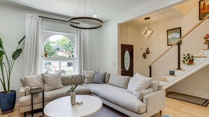 Uma sala de estar com um sofá seccional, uma mesa de centro redonda e uma escada com corrimão.