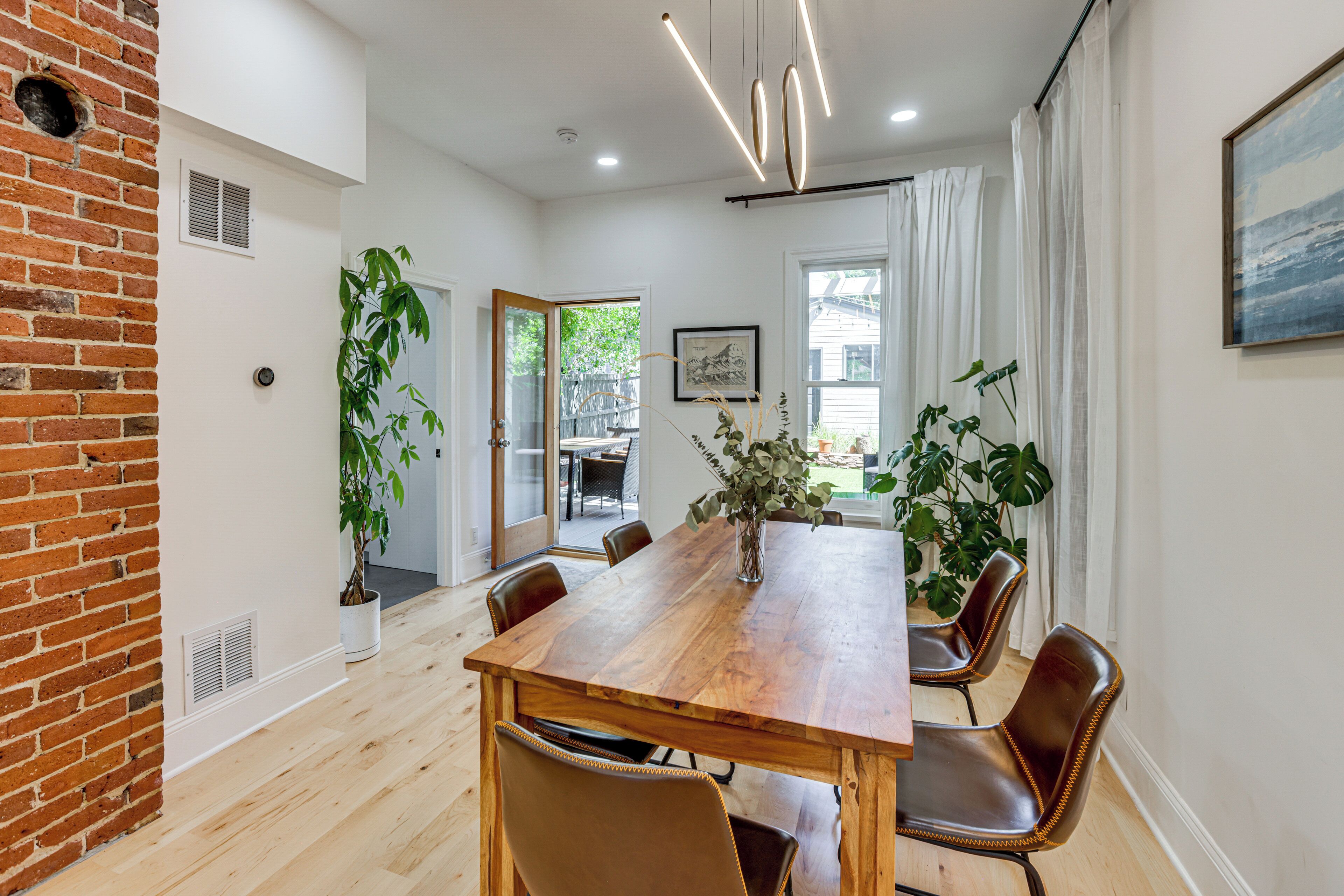 A dining area with a wooden table, leather chairs, potted plants, and a view of the outdoors.