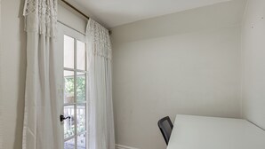 Um quarto com porta branca, uma cadeira branca e vista para um deck externo.
