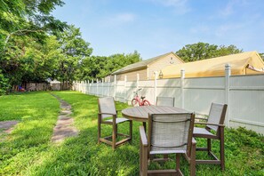 Un jardin avec une table et des chaises en bois, un patio couvert et une clôture blanche.