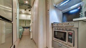 A compact kitchen with a microwave, oven, and a small countertop. - Catskills Airstream! Pavilion & Fire Pit Access (Franklin)