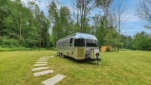 A recreational vehicle parked on a grassy field with a paved path leading to it. - Catskills Airstream! Pavilion & Fire Pit Access (Franklin)