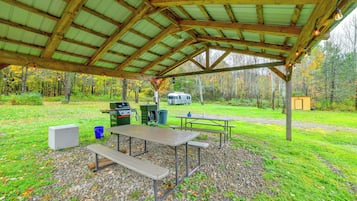An outdoor covered picnic area with picnic tables, a grill, and a portable toilet.