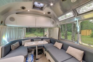 Un intérieur de camping-car compact comprenant un coin repas, un coin cuisine et de grandes fenêtres offrant une vue sur l’extérieur.