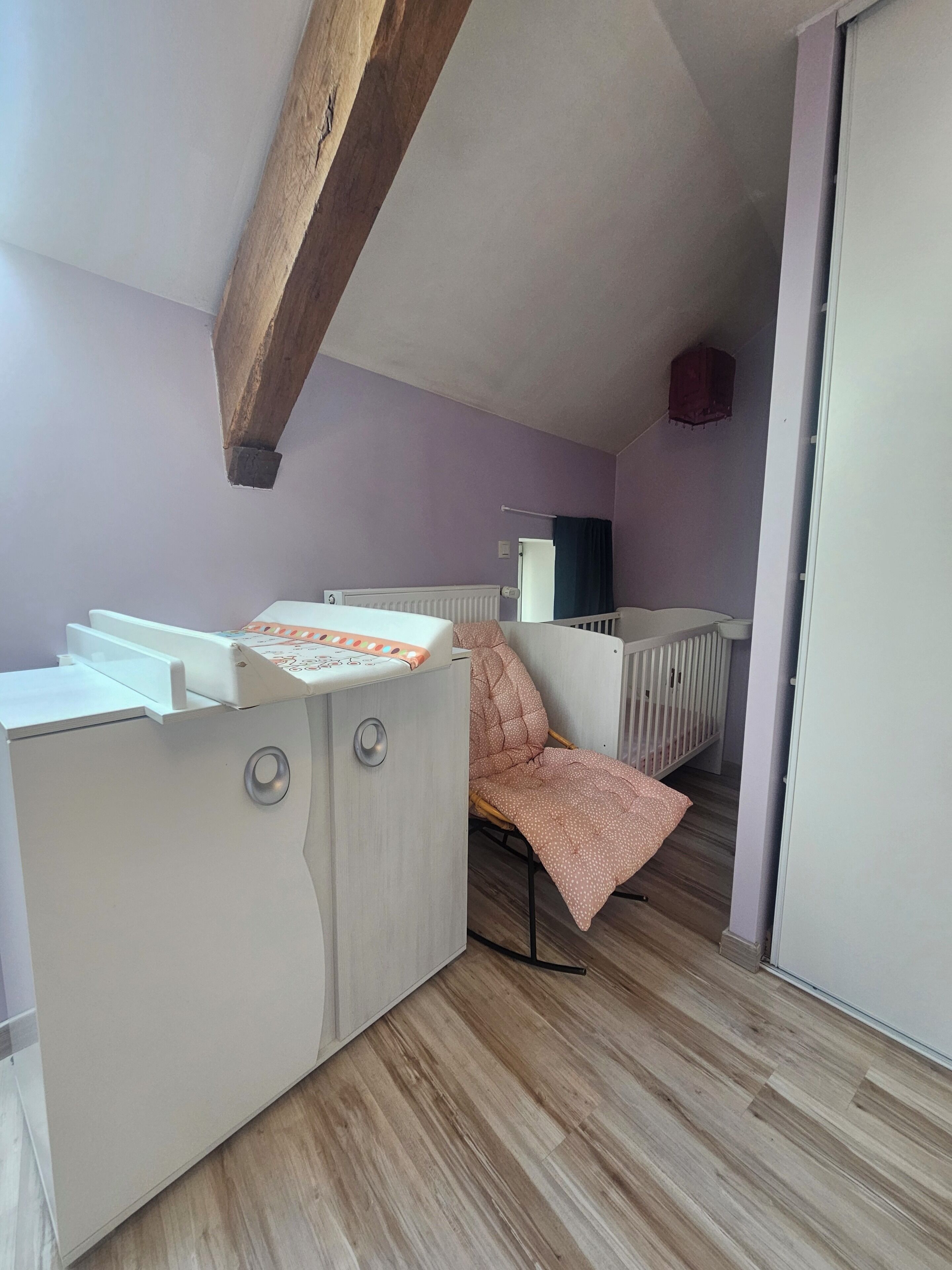 A room with a wooden ceiling, a crib, a changing table, and a wooden floor.