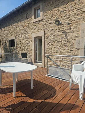 A stone building with a wooden deck, a white table, and a white chair. - Apartment for 6 people in the heart of the Aveyron, 15 minutes from the Lévézou Lakes (Ségur)