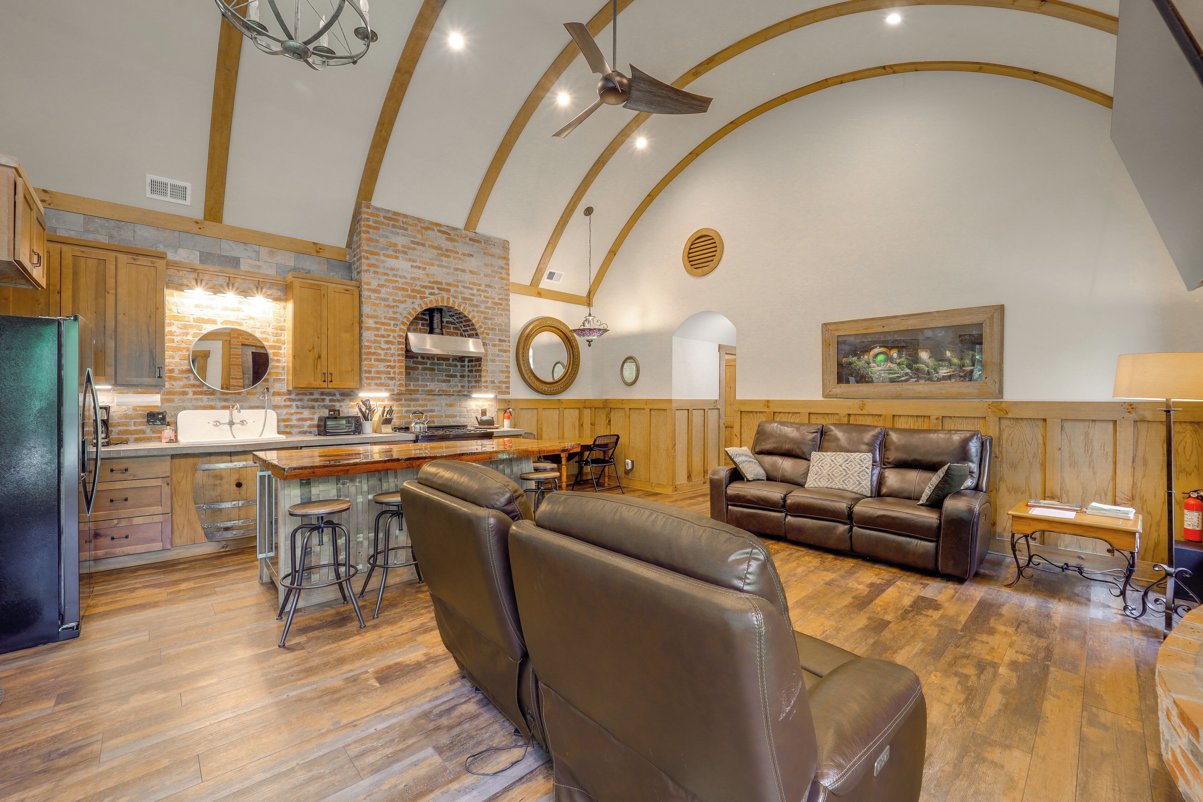 A spacious living area with a leather sofa, a wooden dining table, and a kitchen with a brick wall and wooden beams.