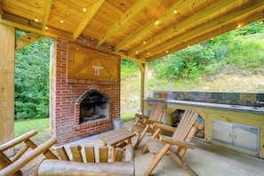 Eine Terrasse im Freien mit Kamin aus Ziegelsteinen, Holzstühlen und einem Grill.