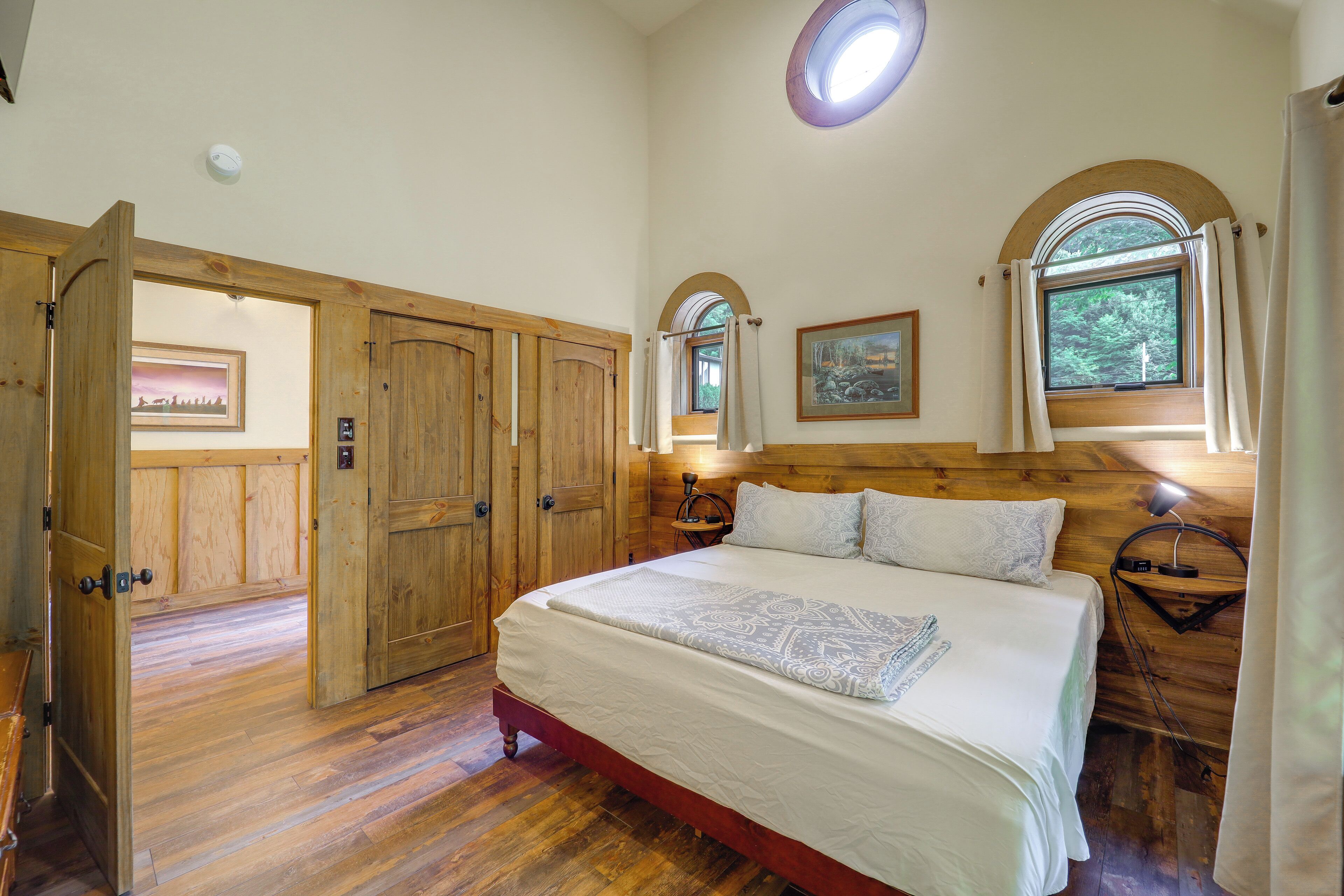 A bedroom with a large bed, wooden wardrobe, and a window with a view of greenery.