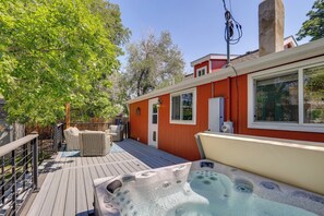 Ein Whirlpool auf einer Holzdielen-Terrasse, ein rotes Gebäude mit Fenstern und eine grüne Umzäunung.
