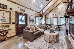 Ein gemütliches Blockhauss-Interieur mit Holzvertäfelung, einem Ledersofa, einem runden Couchtisch und einem Kamin.