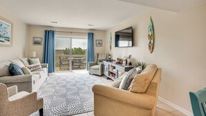 Un salón amplio con un ventanal grande, un televisor de pantalla plana y una zona de comedor con mesa y sillas.