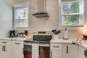A modern kitchen with a stainless steel stove, white cabinetry, and a window with blinds. - Helen Family Home w/ Innsbruck Resort Perks! (Helen)