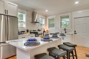Una cocina moderna con armarios blancos, un refrigerador de acero inoxidable, una isla central con cuencos de diseño azul y blanco, y taburetes de bar.