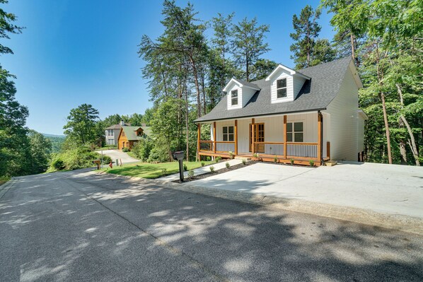 Een tweelaags huis met een veranda, omringd door bomen en een heldere lucht.