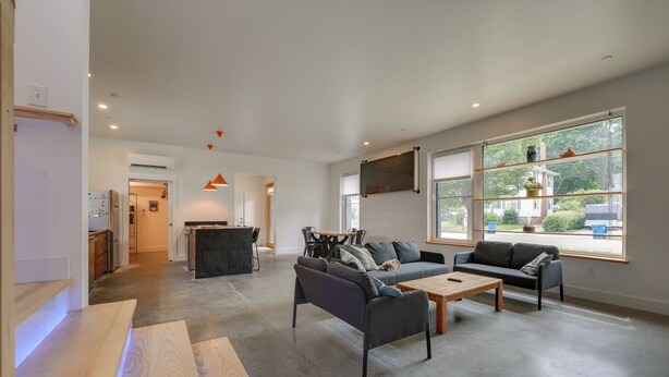 A spacious living area with a sofa, a coffee table, and a TV mounted on the wall. - Shop, Dine, Walk to Deering Oaks! Family Getaway (Portland)