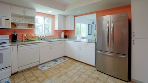 Una cocina moderna con armarios blancos, un refrigerador de acero inoxidable y una cafetera.