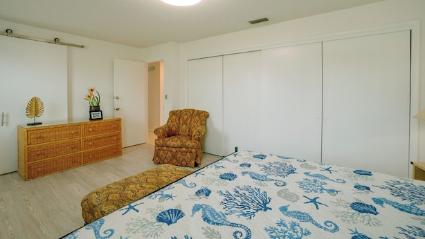 Un dormitorio con cama, una silla, cómoda y armario.