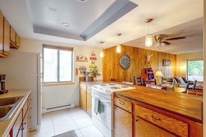A kitchen with wooden cabinets, a stove, and a dining area with a table and chairs. - Fraser Condo w/ Pool & Hot Tubs: Close to Trails! (Fraser)