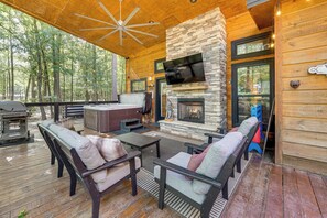 Un espacio de estar al aire libre cubierto con chimenea de piedra, televisor y parrilla.